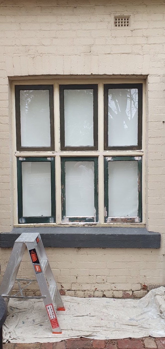 A timber sash window part-way through painting, with the glass masked