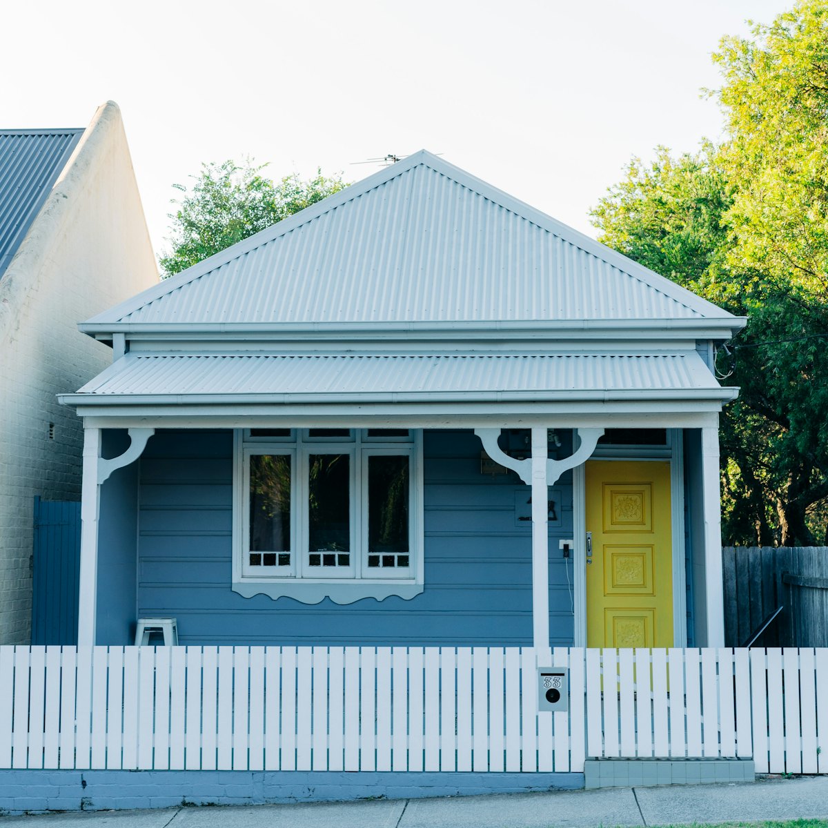 A freshly painted blue weatherboard cottage with a yellow front door